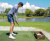 Person practicing golf on a driving range with a lake and trees in the background